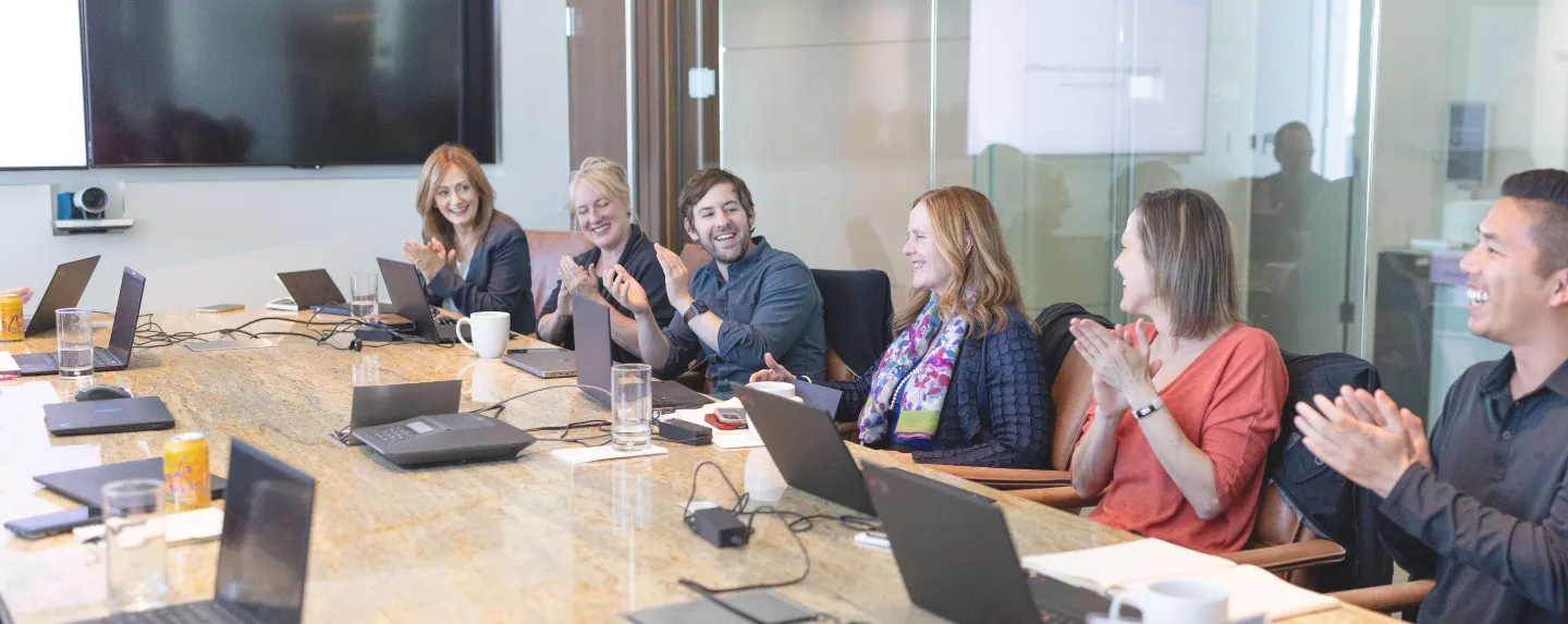 Photo of four team members sitting around a conference table smiling and clapping.