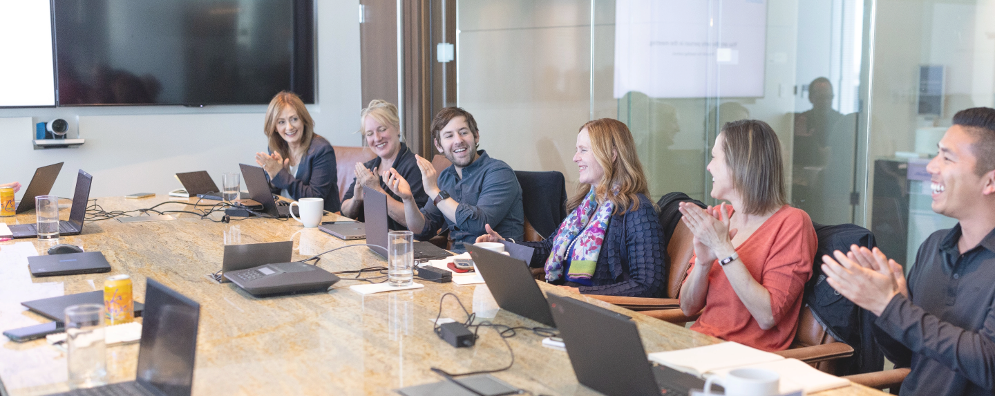 Photo of four team members sitting around a conference table smiling and clapping.
