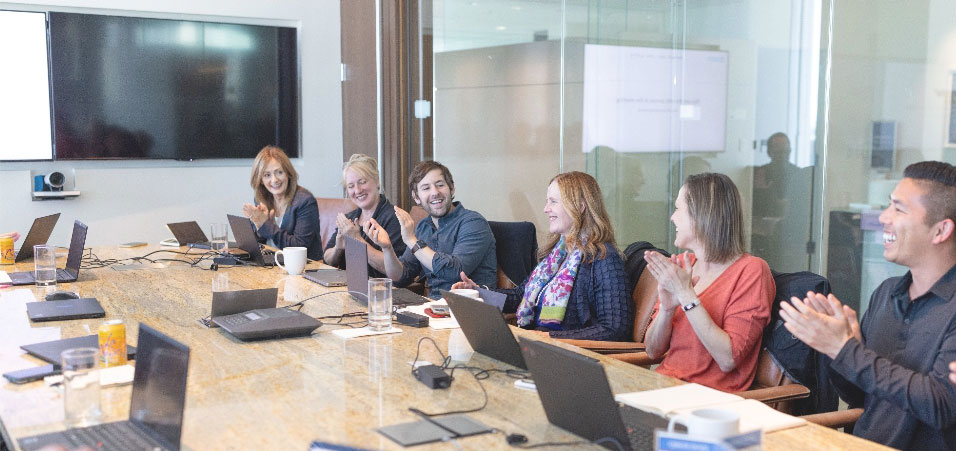 Photo of four team members sitting around a conference table smiling and clapping.