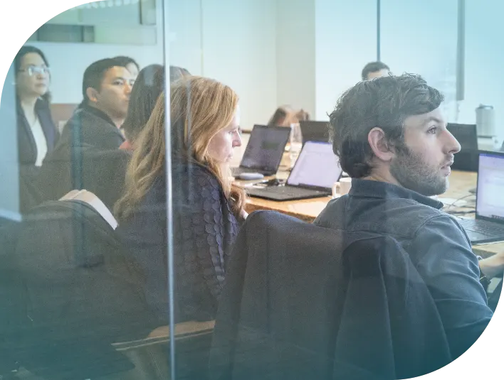 Photograph looking through a glass window into a conference room with Apogee team members sitting around a table